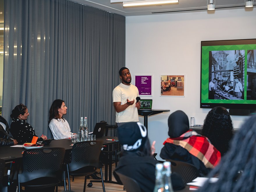 a person stands up in a room of seated people and talks to them