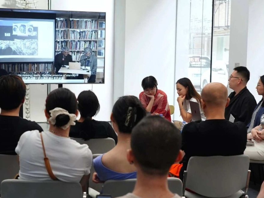 A group of people sit in a discussion while someone leads with a powerpoint