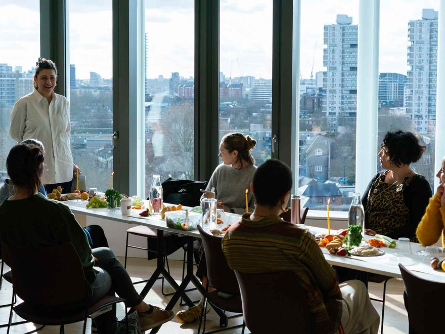 People sit at a long table in front of a large window with views of a city