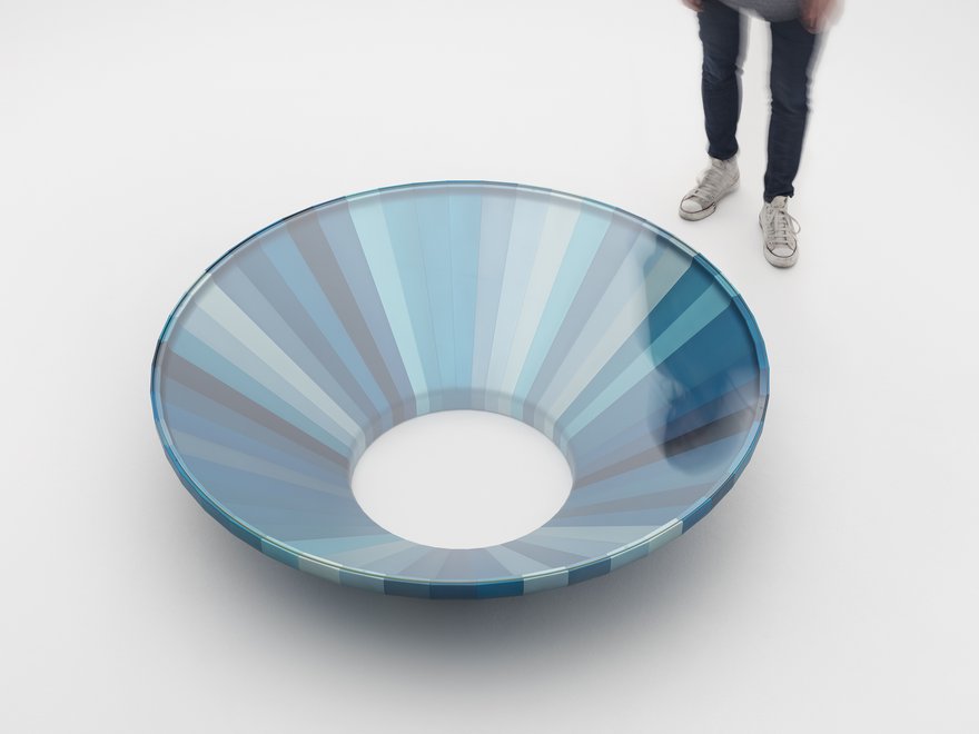 A large circular 'donut' shaped artwork made from striped glass in shades of blue.