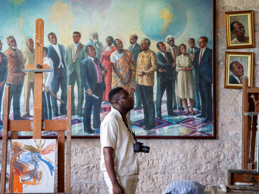 A man with a camera round his neck stands in front a big oil painting