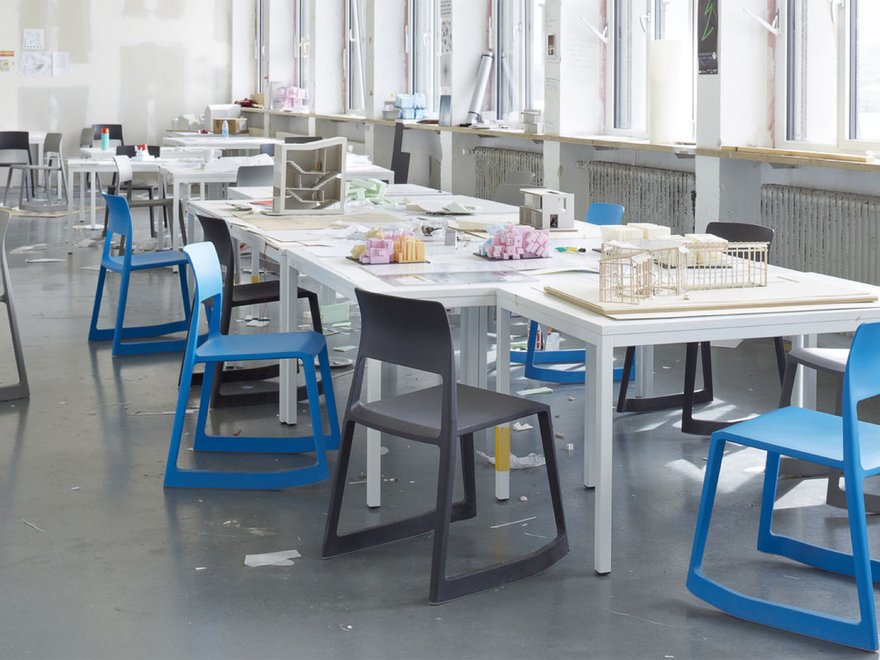 Design studio with white tables, colourful chairs, and architectural models scattered across a bright, window-lit workspace.