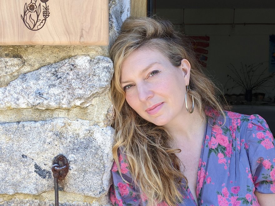 A women with blonde hair leans against a stone wall